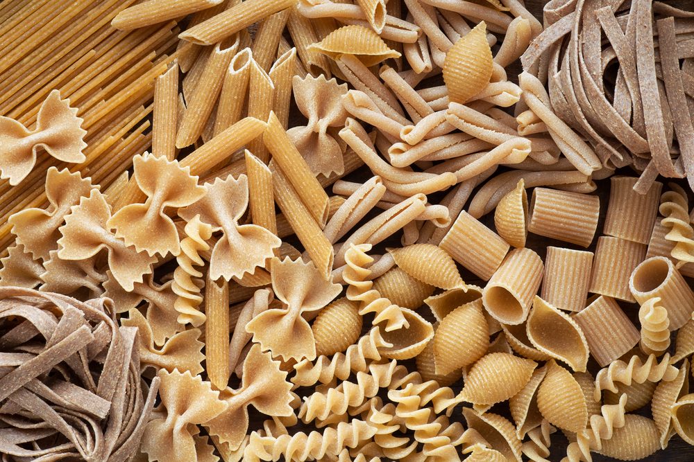 Assorted uncooked pasta sits closely packed, showcasing various shapes like penne, farfalle, fusilli, and shells in a top-down view.
