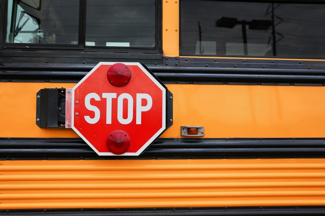 Stop sign extends from a yellow school bus, warning vehicles in a parking lot setting.