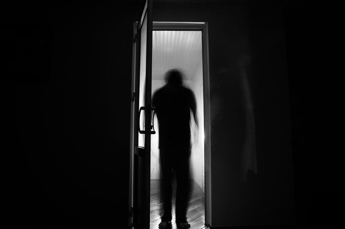 Silhouette of an unknown shadow figure on a door through a closed glass door. The silhouette of a human in front of a window at night. Scary scene halloween concept of blurred silhouette of maniac.