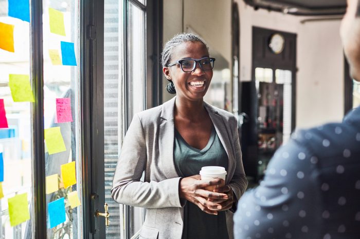 Smiling young woman talking with her colleague while having coffee at office. Business people having a casual talk during coffee break.