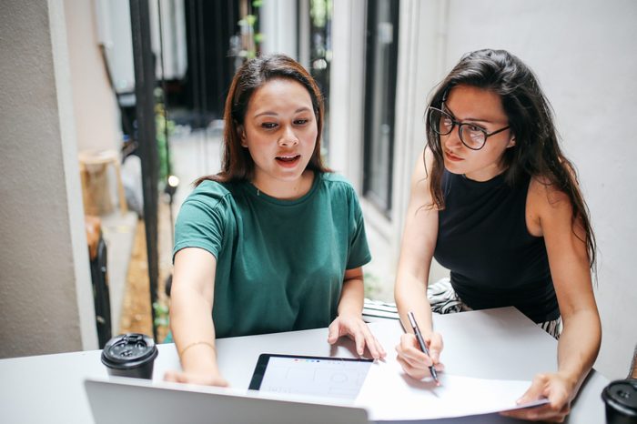 Two young women staying late in the office, finishing up with work at the laptop.