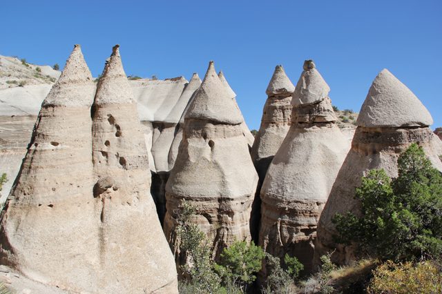 Cone-shaped rock formations stand prominently amid sparse vegetation under a clear blue sky.