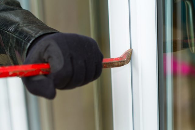 Burglar wearing black clothes and leather coat breaking in a house