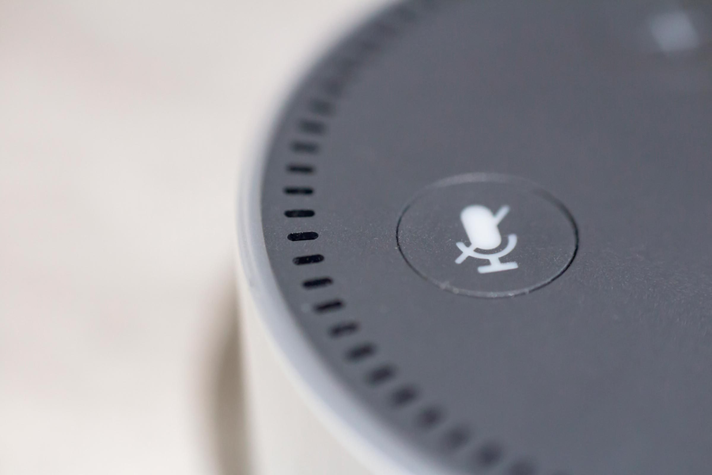 Smart speaker top with a microphone symbol, indicating mute, sits on a blurred surface.