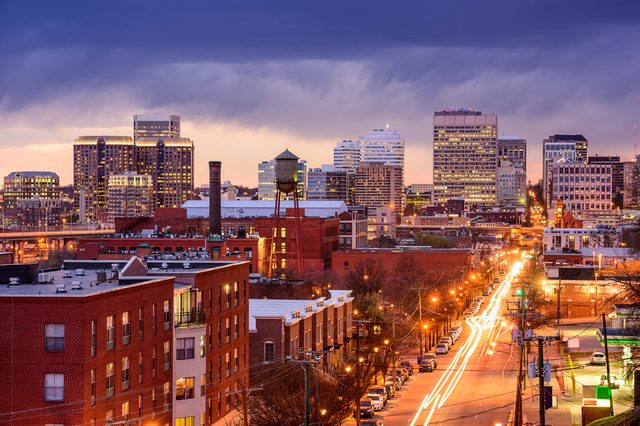 City skyline; buildings illuminated at twilight; cars create light trails on a busy street.