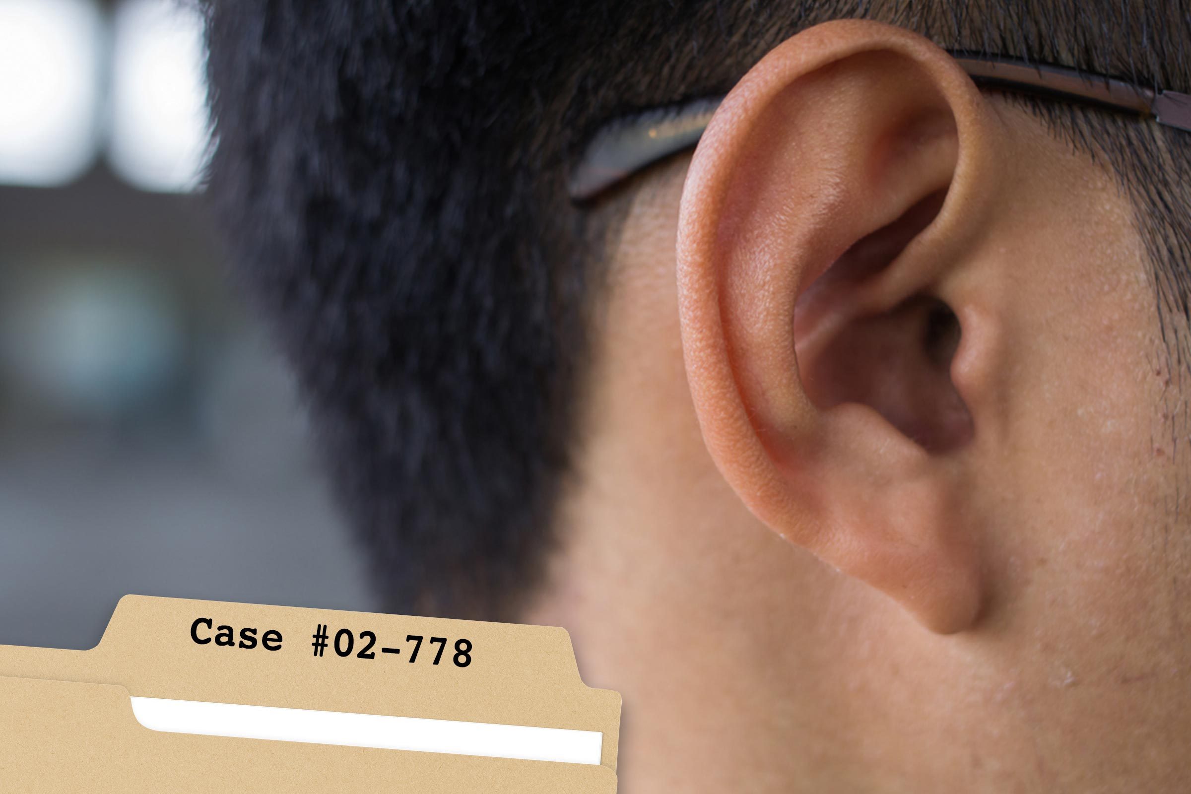 An ear is partially covered by glasses, with text "Case #02-778" on a file folder in the foreground.
