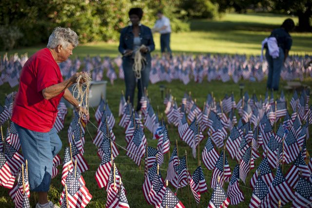 A person arranges small American flags in a grassy field, surrounded by others participating in the task.