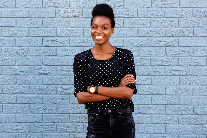 Portrait of attractive young african woman standing with her arms crossed against gray brick wall