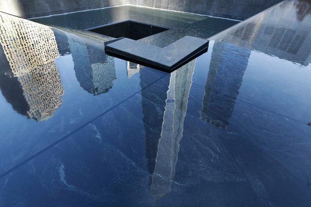 Pool reflecting skyscrapers, with water cascading into a square void; surrounded by stone surfaces.