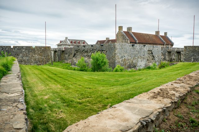 Stone fortress stands surrounded by a lush, grassy field under a cloudy sky.