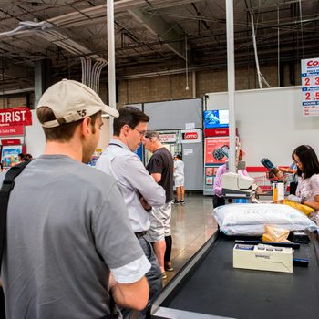 Customers wait as a cashier scans items at a retail checkout counter in a warehouse store.