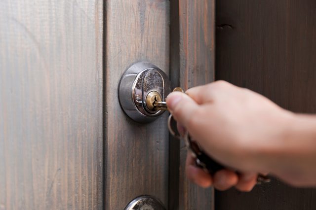 Hand turning key in door lock on a wooden door.