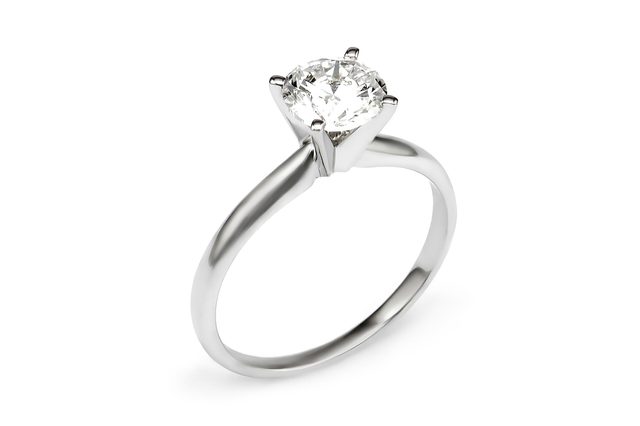 A silver ring displays a large, round diamond atop its band, set against a plain white background.