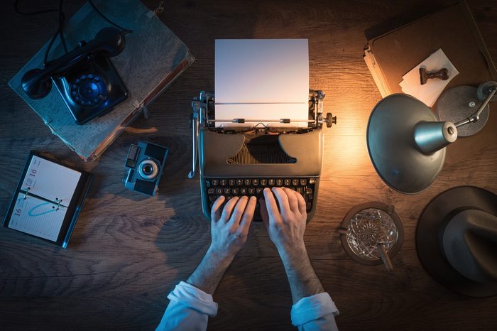 Vintage journalist's desk 1950s style, he is working and typing on his typewriter late at night, top view