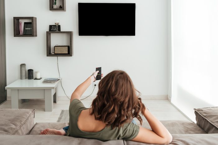 Back view of casual woman sitting on sofa and watching TV in home