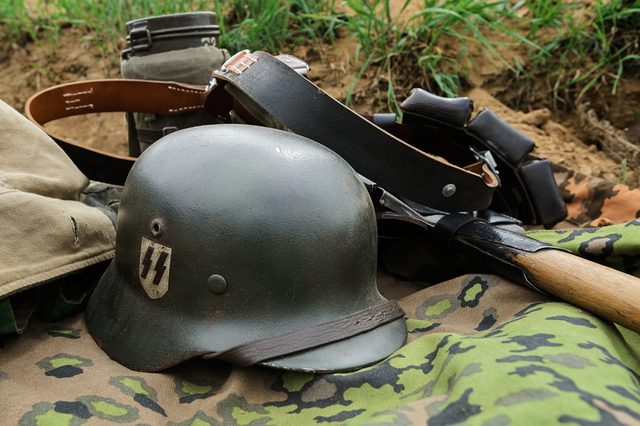Helmet rests on camouflage fabric amid military gear in grassy field.