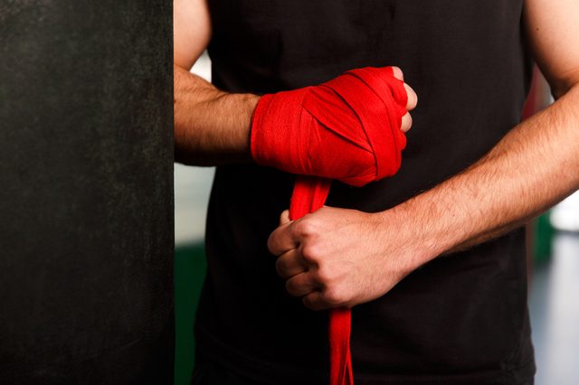 Arm wraps red boxing hand wraps around wrist in a gym setting, preparing for training or competition.
