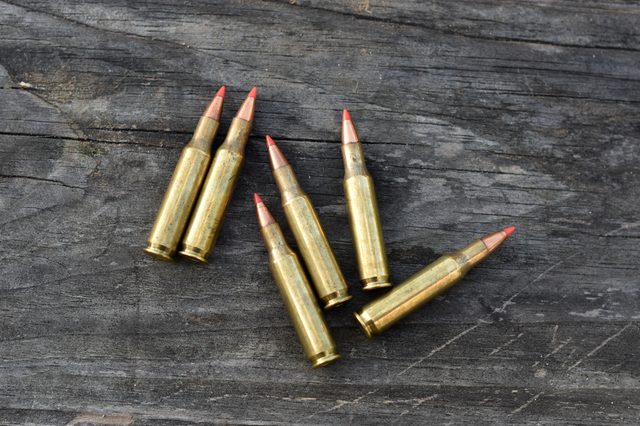 Bullets lie scattered on a weathered wooden surface, positioned with their pointed ends facing varying directions.