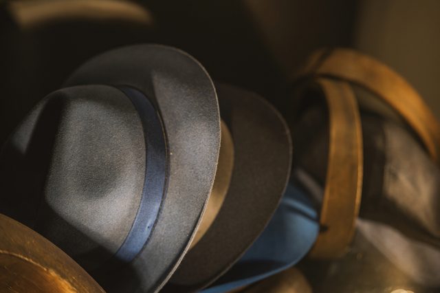 Hats lie stacked casually in soft light, surrounded by brown fabric and leather.