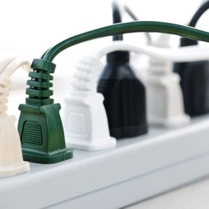 Power strip hosts various colored plugs inserted, lying on a smooth white surface in a well-lit indoor setting.