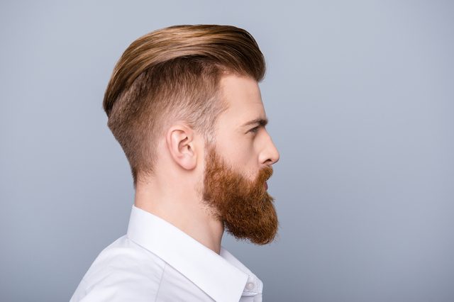 Side profile of a bearded man facing right, wearing a white shirt against a plain gray background.
