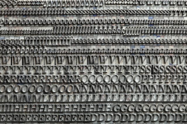Metal letterpress blocks display letters in rows, arranged neatly in a dense, orderly pattern, showcasing various fonts and characters.