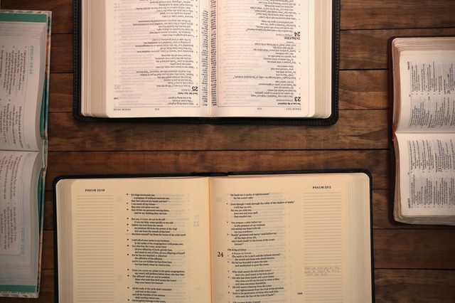 Open Bibles lying on a wooden table, displaying different chapters and verses, surrounded by additional opened books.