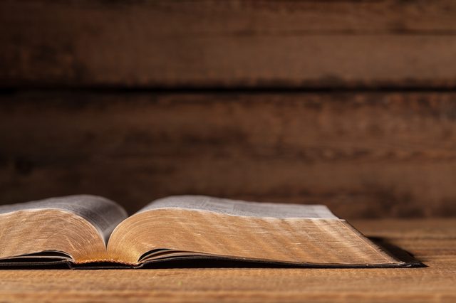 An open book rests on a wooden surface against a blurry wooden background, pages slightly curled.