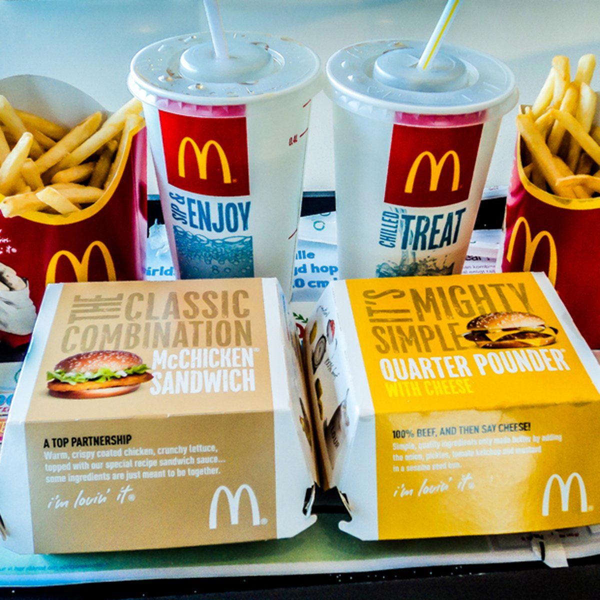 Two McDonald's burgers in boxes, next to fries and drinks, on a tray. Text includes "McChicken Sandwich" and "Quarter Pounder with Cheese."