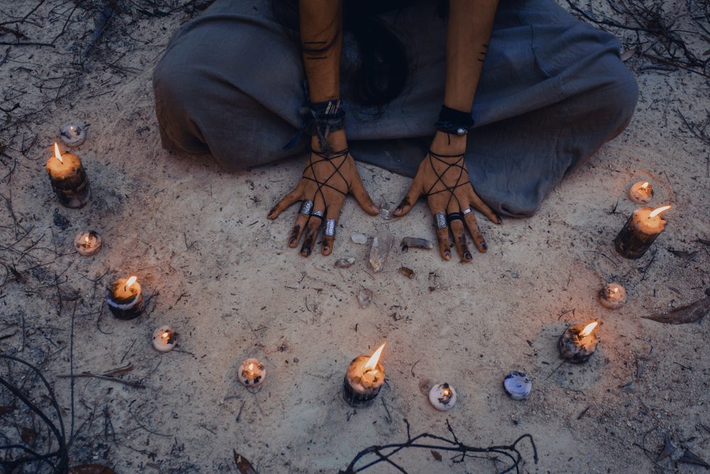 Witchs hands from above with candles deep in forest.