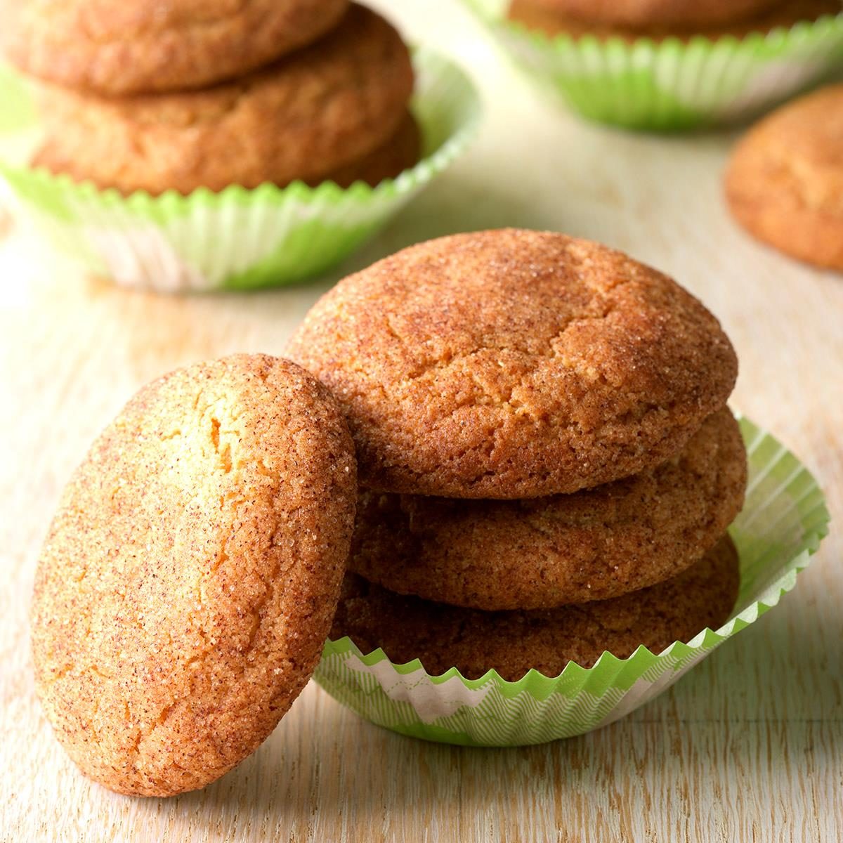 Cookies stacked inside green paper cups on a wooden surface, with more cookies in the background.