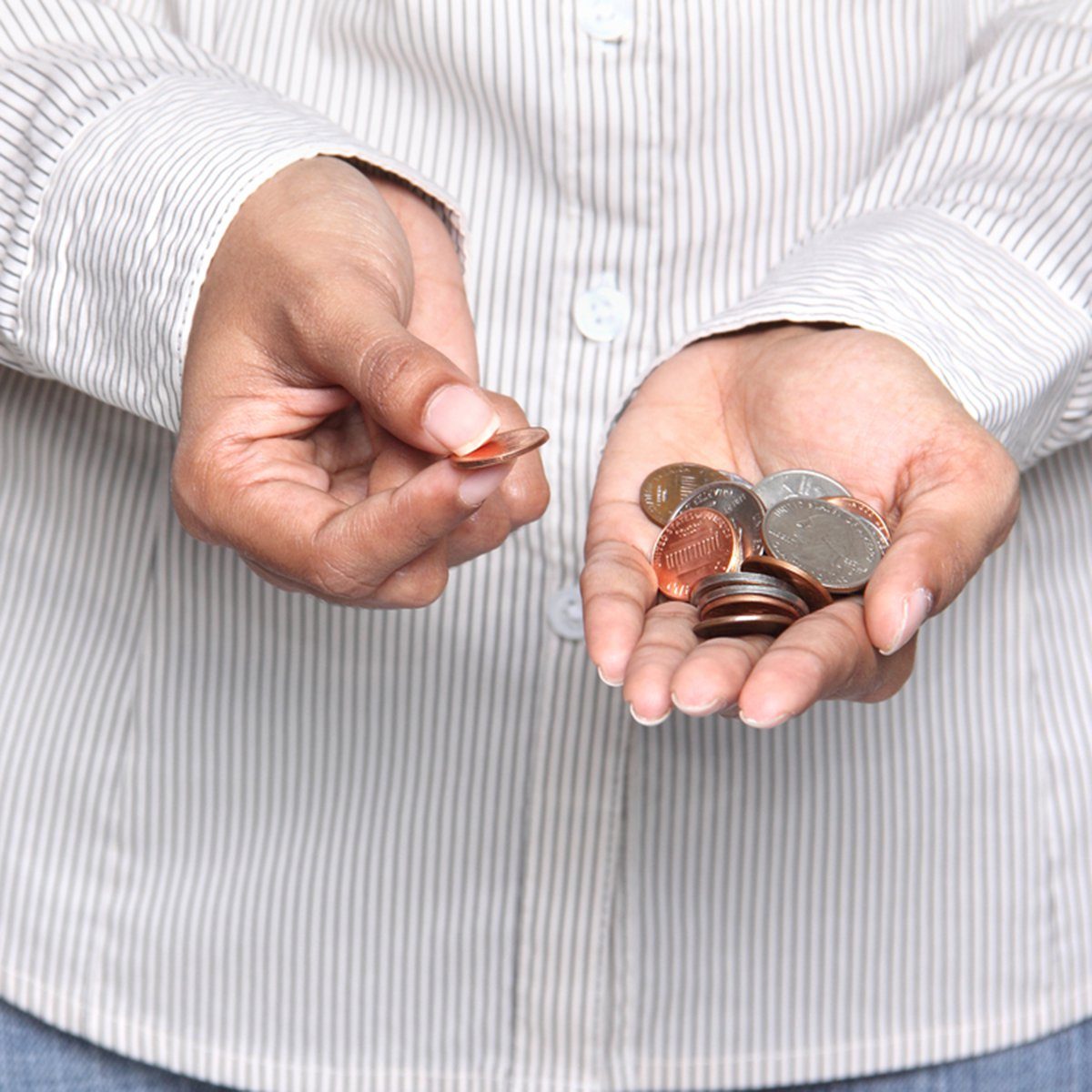 Hands holding and counting assorted coins, standing against a background of a vertical striped shirt.