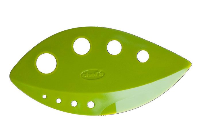 Green leaf-shaped tool, featuring various round holes, is stationary against a plain white background. The word 