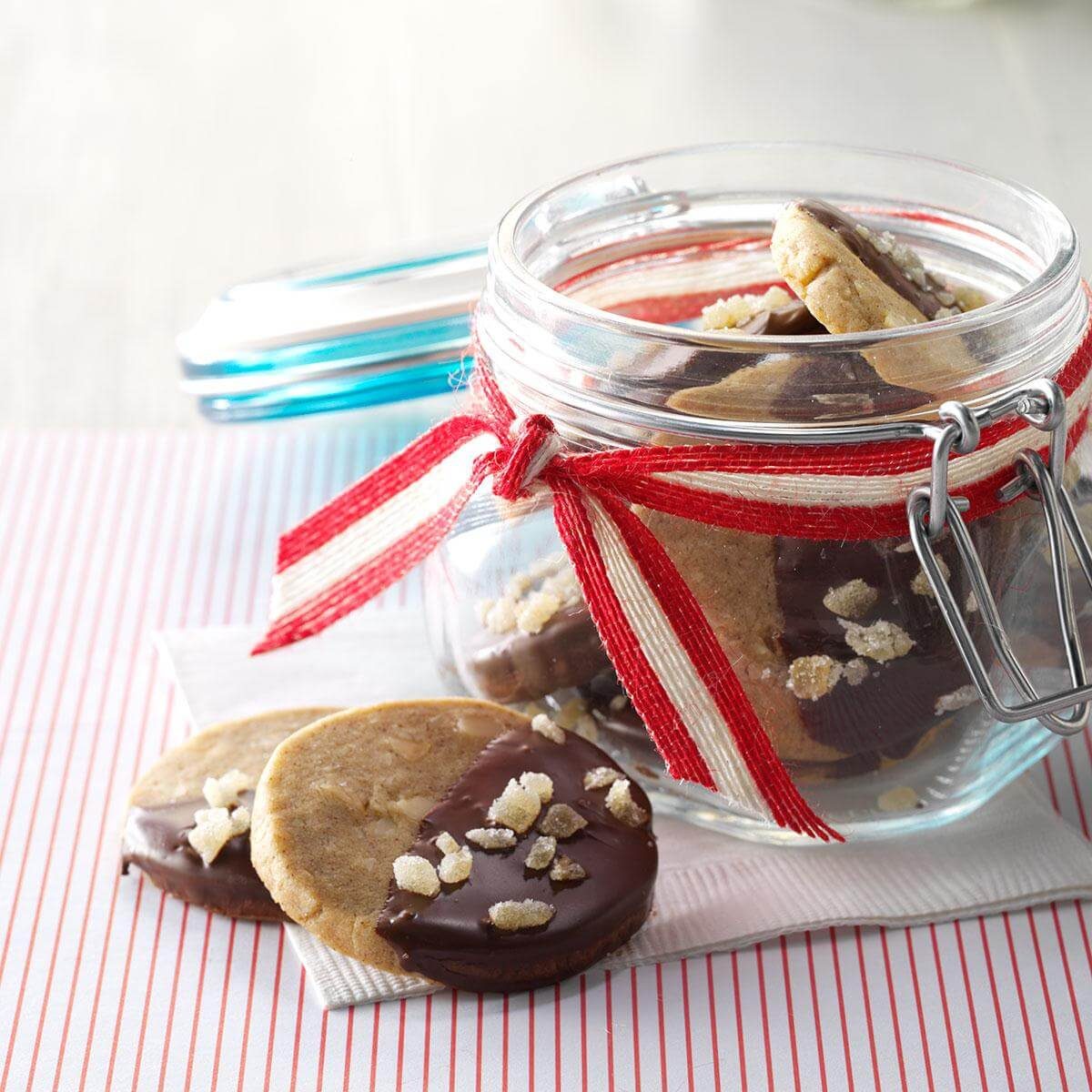 Cookies rest in a jar adorned with a red ribbon, surrounded by a striped napkin and table, creating a cozy presentation.