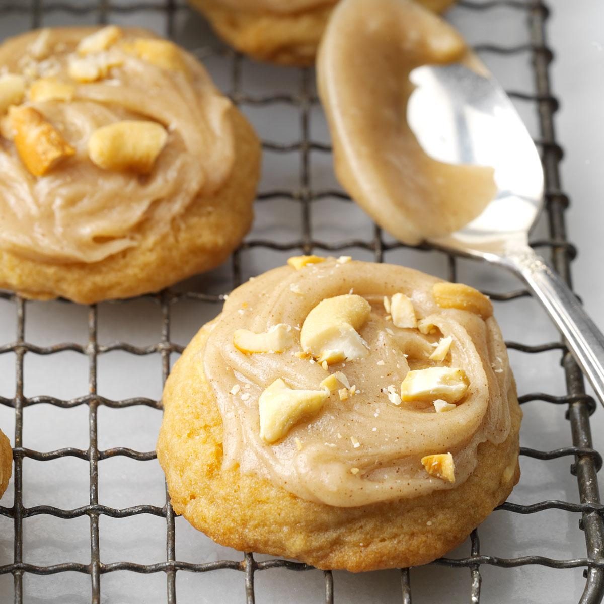Cookies topped with frosting and nuts rest on a wire cooling rack, with a spoon nearby holding more frosting.