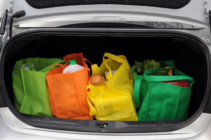 Four colorful eco-friendly shopping bags filled mostly with groceries in the trunk of a car.