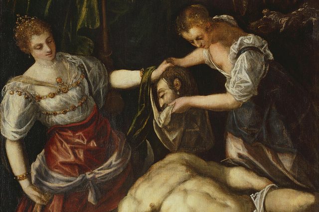 Two women hold a severed head, dressed in ornate clothing, within a dimly lit, dramatic setting.