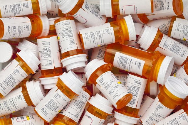 Prescription bottles scattered, displaying labels and warnings; white caps contrast orange containers, creating a busy, cluttered appearance.