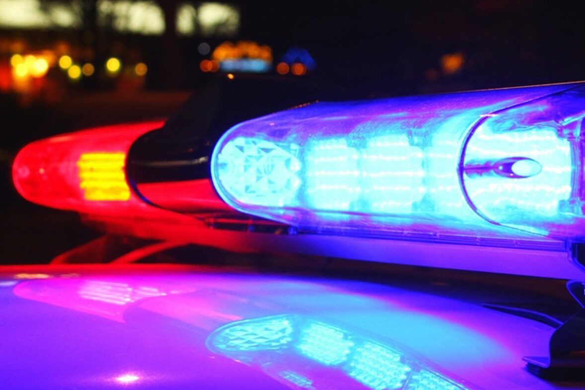 Police lights flashing red and blue atop a vehicle, illuminating the dark urban background.