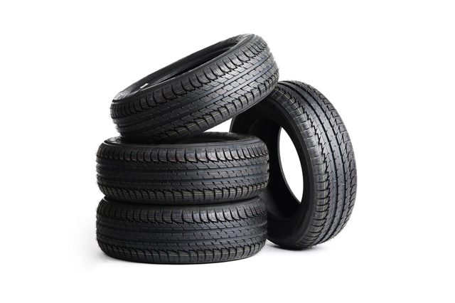 Four black car tires stacked, one leaning on others, with visible treads, against a white background.