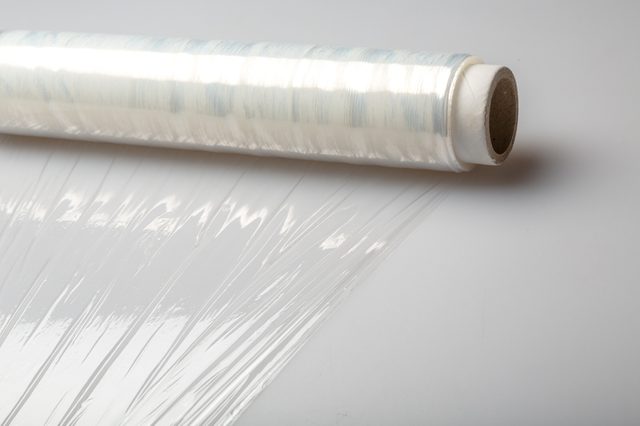 A roll of clear plastic wrap unfurls across a smooth, light-colored surface.