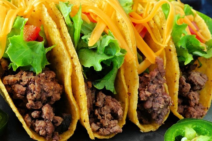 Group of hard shelled tacos with ground beef, lettuce, tomatoes and cheese close up