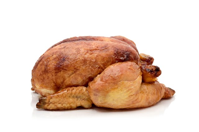 A whole roasted chicken rests on a reflective white surface, showcasing golden-brown crispy skin with no additional background elements.