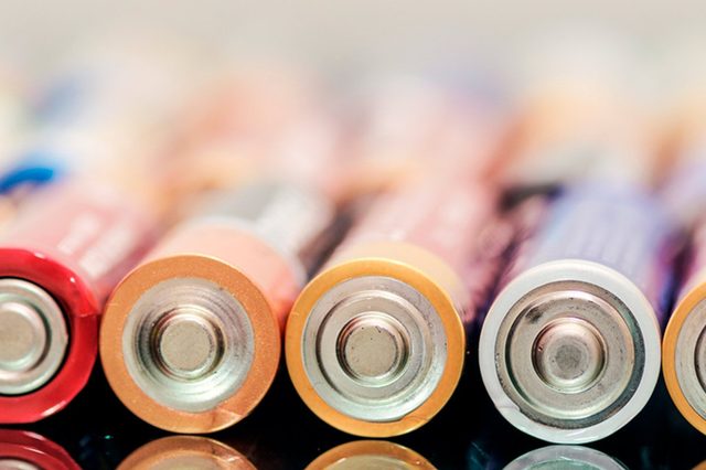 Batteries rest horizontally, lined up in a row, on a reflective surface, showcasing their metallic ends in a softly lit environment.