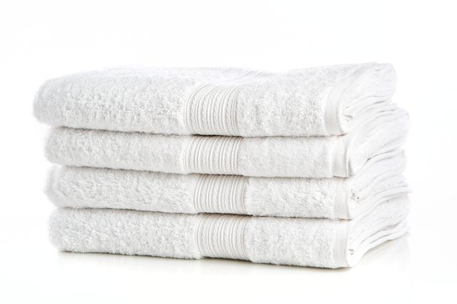 Four neatly folded white towels stacked on a glossy surface with a soft, clean appearance.