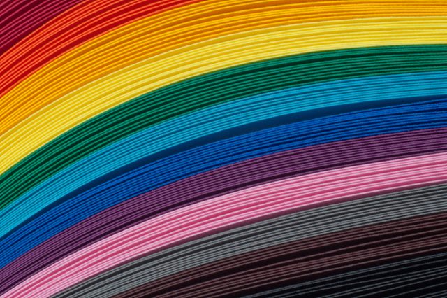 Colorful paper sheets stack horizontally, creating rainbow stripes against a smooth, uniform background.