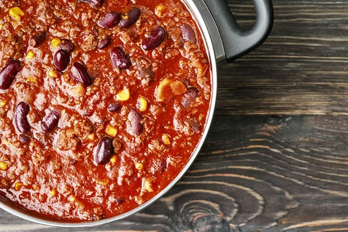 Saucepan with delicious chili con carne on wooden background
