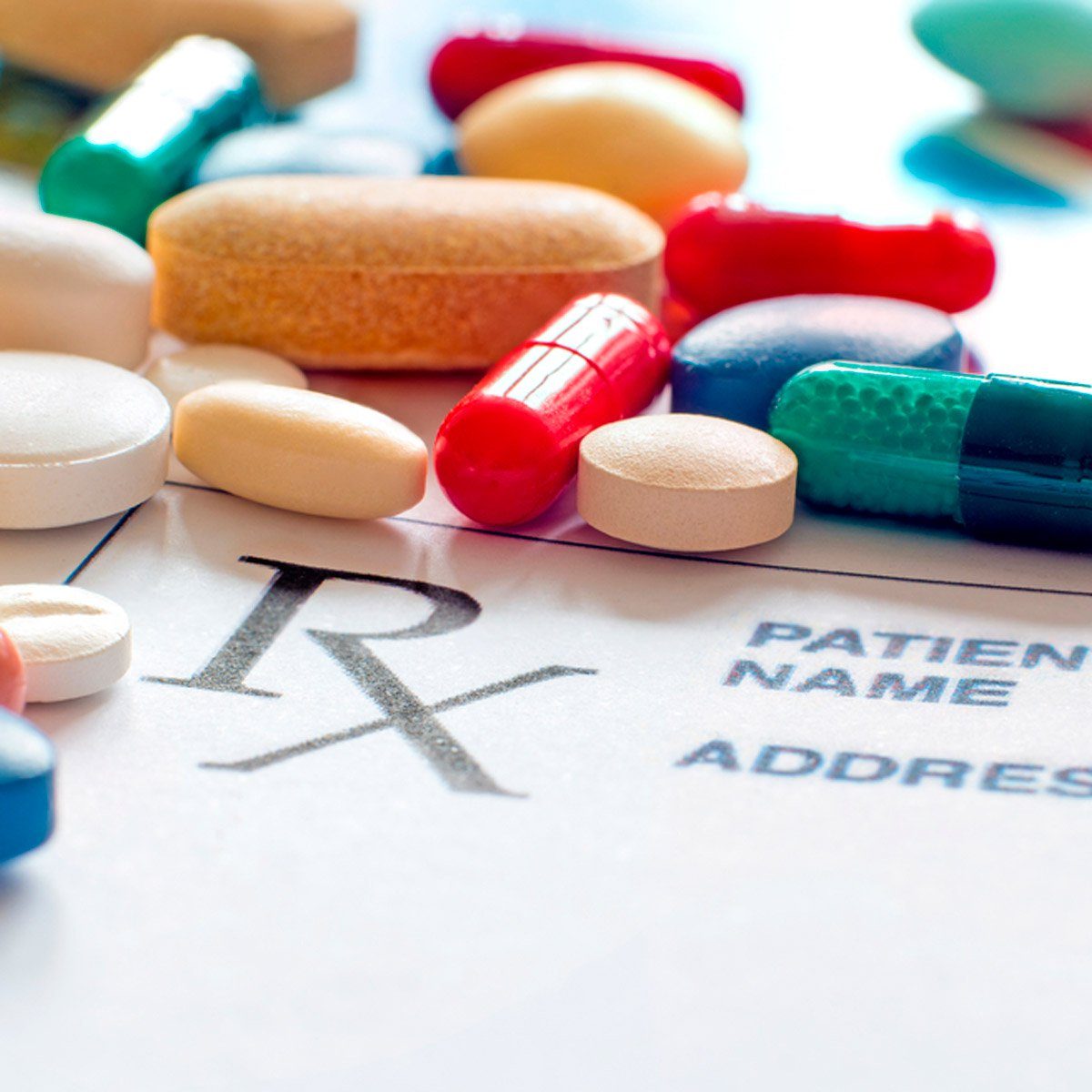 Pills scattered across a prescription form with printed text "Rx," "PATIENT NAME," and "ADDRESS" visible, suggesting medication context.