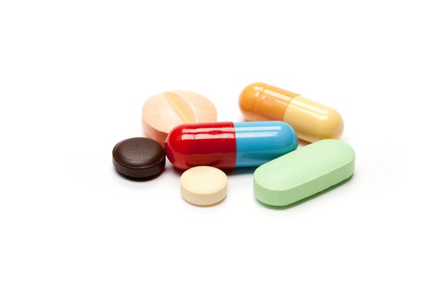 Various pills rest together; vibrant colors include red, blue, green, brown, and orange, creating a scattered arrangement on a white background.