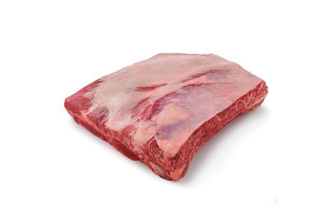 A slab of marbled raw beef rests on a plain white background, showcasing intricate fat patterns.